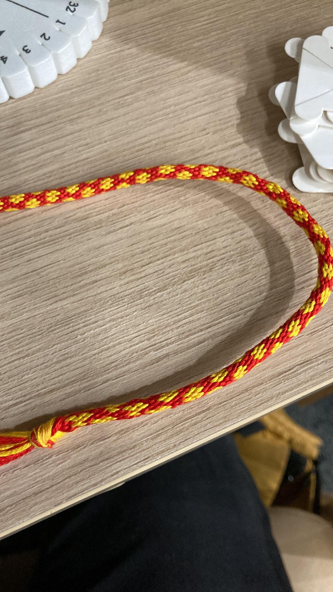 A red woven kumihimo cord with decorated yellow flowers.